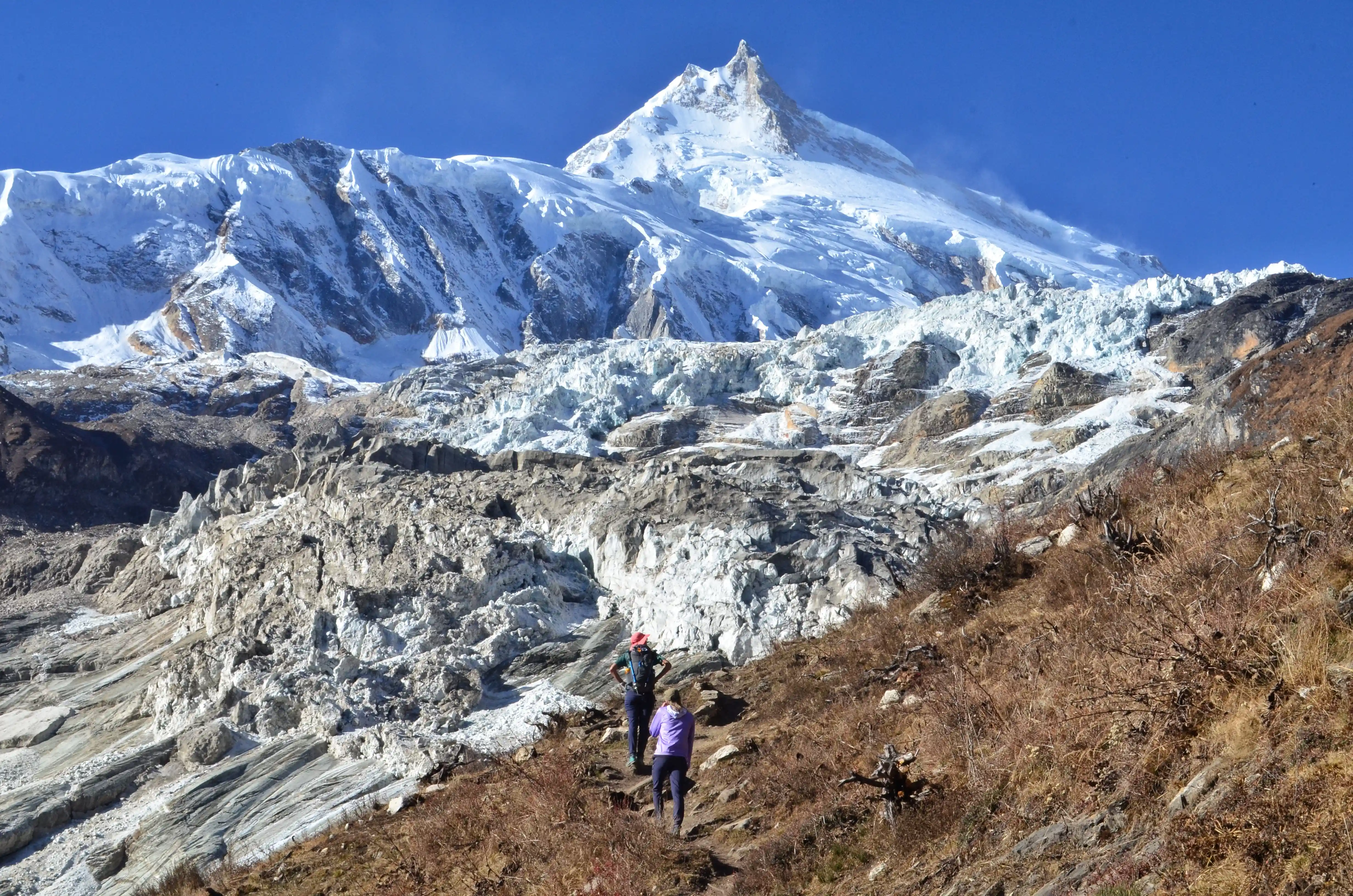 Trekkers walking on the Manaslu Circuit trail in Nepal with views of high Himalayan peaks