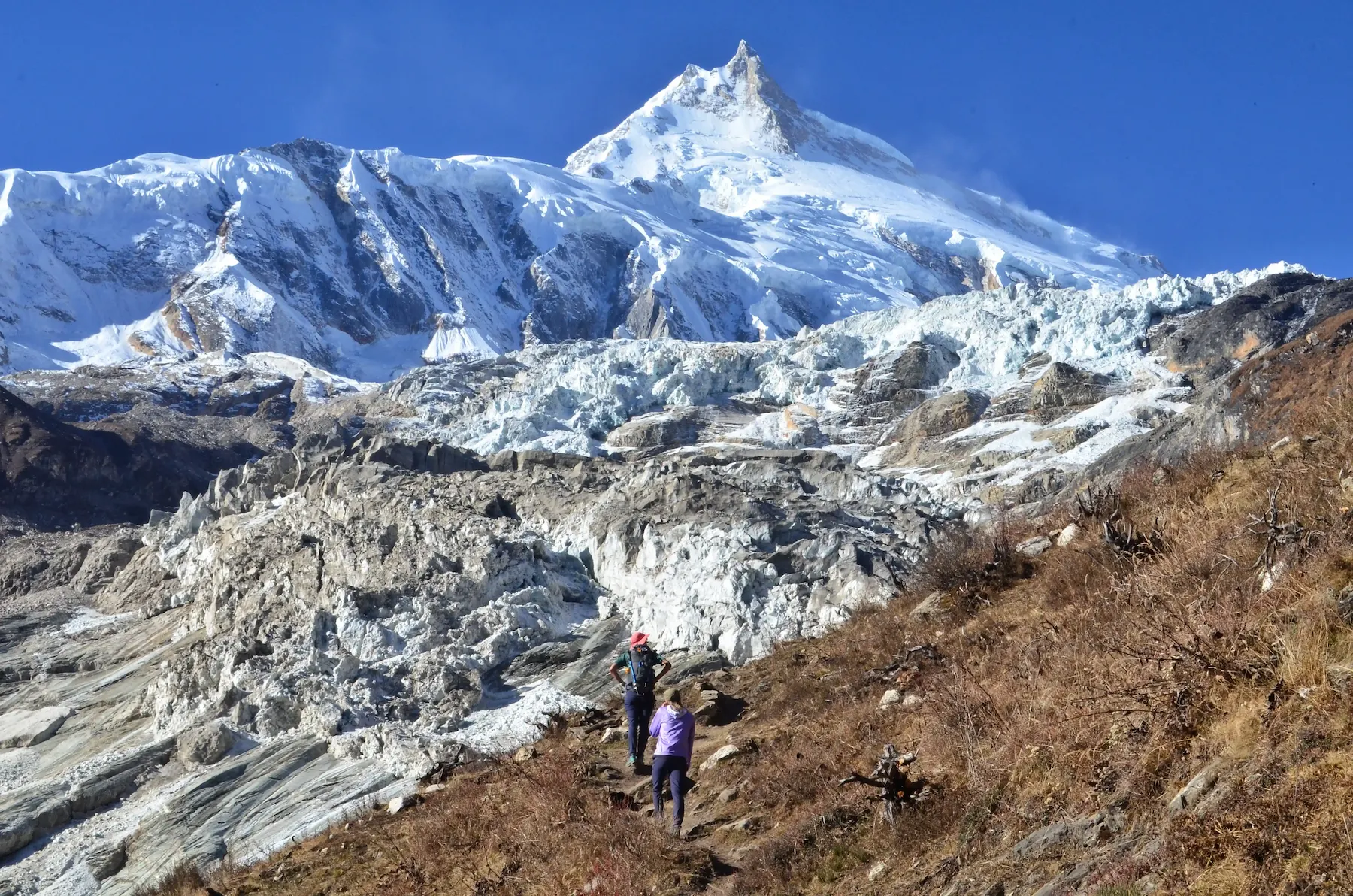 Trekkers walking on the Manaslu Circuit trail in Nepal with views of high Himalayan peaks